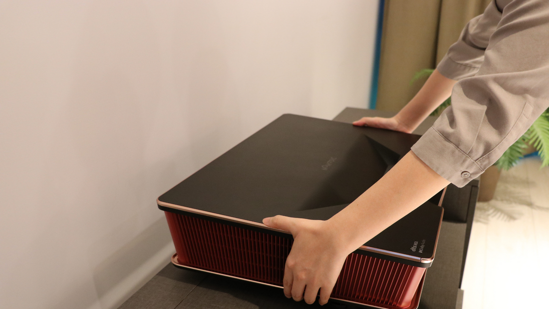 A person placing the ultra short throw 4K projector P2000 in front of the wall, on a cabinet